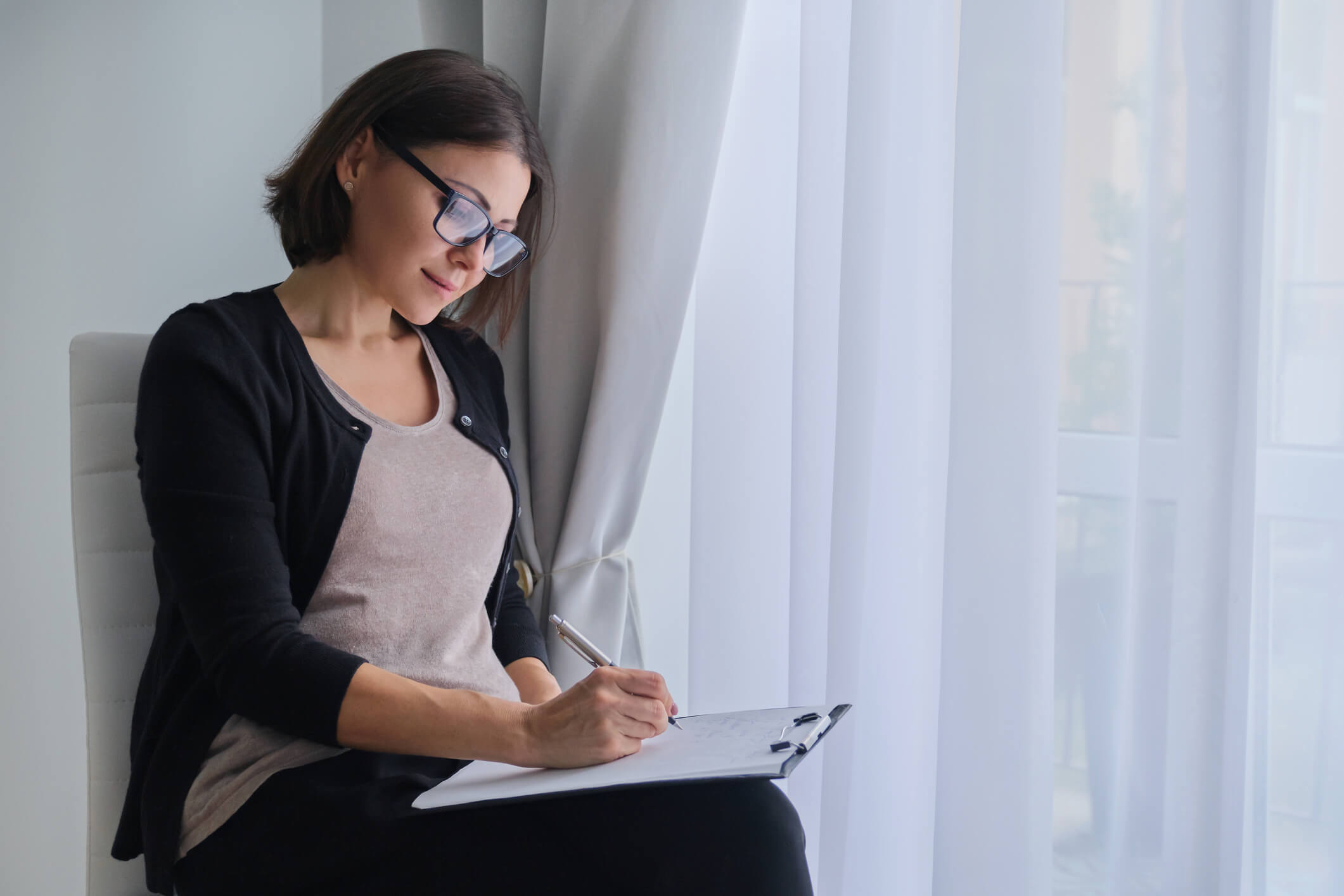 woman social worker, psychologist sitting near the window with clipping board